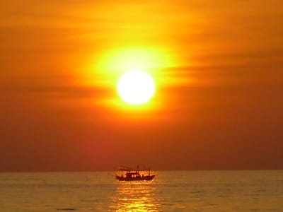 Fishing boat on ocean in sun setting.