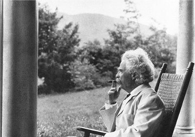 A famous man sitting in a rocking chair on a porch with a pocket notebook.