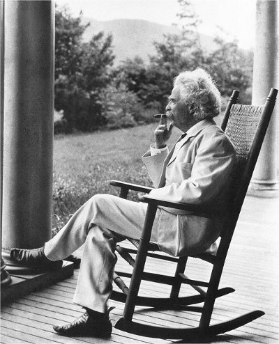 A famous man sitting in a rocking chair on a porch with a pocket notebook.