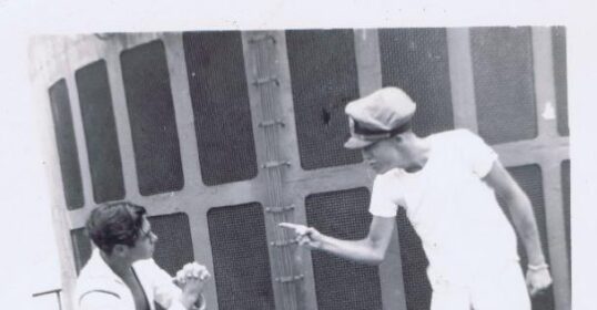 Two manly sailor men fighting in front of a ship.