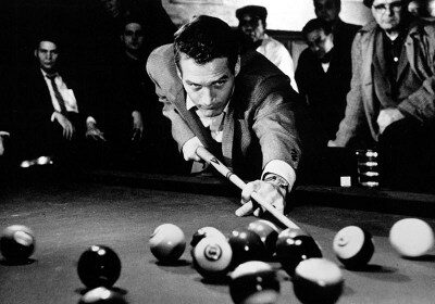 A man, potentially Minnesota Fats, playing pool around a billiard table.