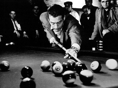 A man, potentially Minnesota Fats, playing pool around a billiard table.
