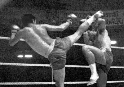 Two men engaging in Muay Thai, Thailand's National Sport, in a boxing ring and kicking each other.