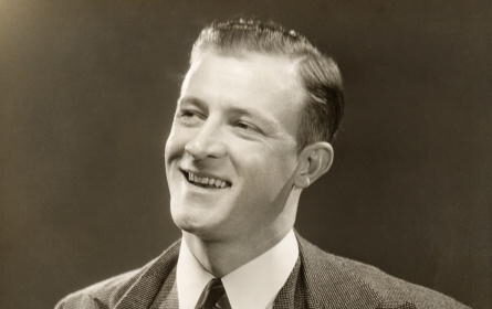 A fully present man in a suit, captured in a black and white photo, with a genuine smile on his face.