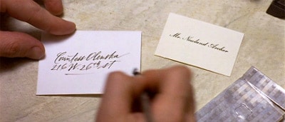 A person using a calling card to write a name on a piece of paper.