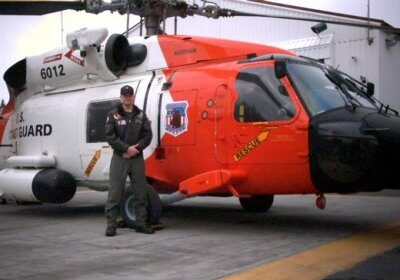 A Coast Guard Helicopter Flight Mechanic standing next to an orange and black helicopter.
