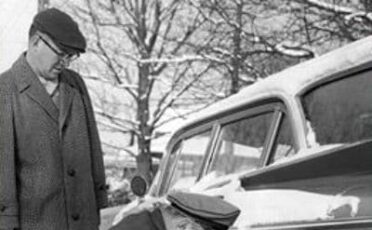 Two men winterizing a car in the snow.