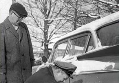 Two men winterizing a car in the snow.
