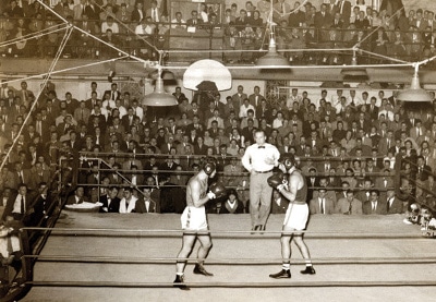 Two amateur men in a boxing ring in an old photograph.