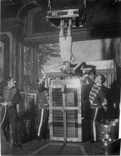 Harry Houdini hanging upside down getting lowered into container.