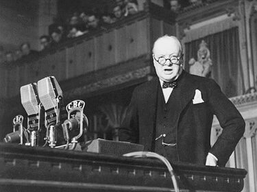 A man in a suit demonstrating classical rhetoric while standing in front of a microphone.