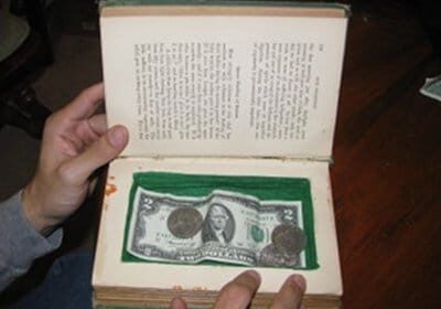 A person holding an open book with a secret compartment for hiding money.