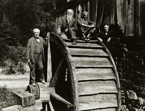 Three men demonstrating the power of cooperation as they stand on top of a water wheel together.