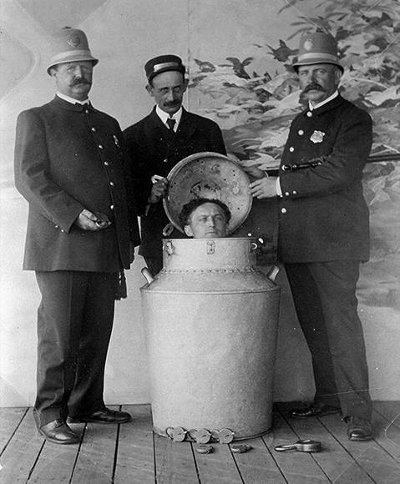 Three men locking Harry Houdini in milk can for magic trick. 