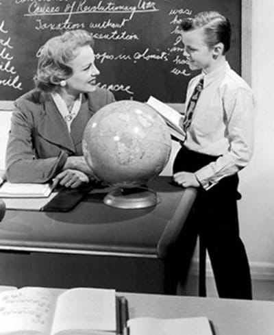 Boy talking to his teacher while holding a book.