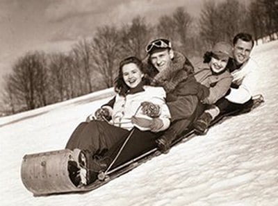 Couples smiling while sledding down on snowy hill. 