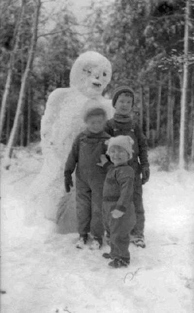 Kids posing with snowman in woods.