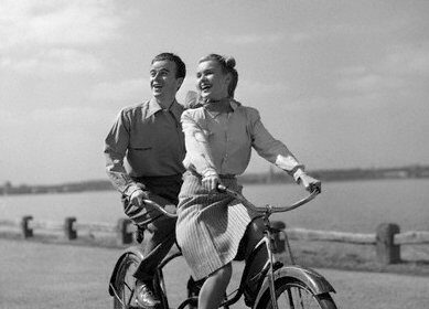 Memorable black and white photo of a man and woman riding a tandem bicycle.
