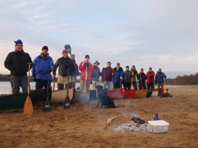 Group of men posing with canoes paddles on beach. 