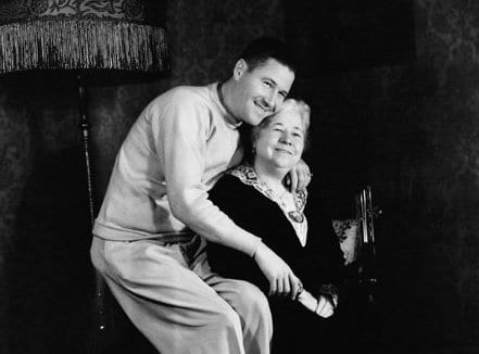 A black and white photo of a man and woman sitting on a chair, depicting a mother and man in a loving relationship.
