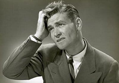 A black and white photo of a man with his hand on his head, showcasing an expression of exasperation.