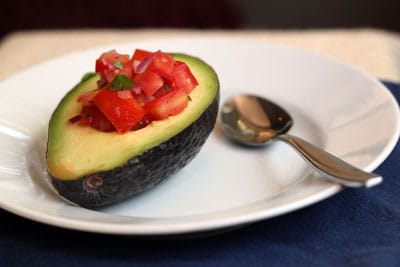 Avocado with tomatoes salad in the plate with spoon. 