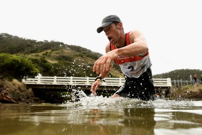 A man participating in mud sprints near a bridge.