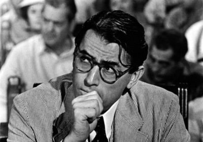 Atticus Finch, a man in glasses, sitting at a desk while imparting important lessons.