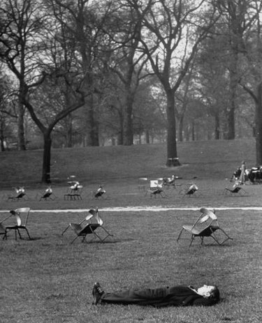 A man is unleashing his power during a relaxing nap in the park, surrounded by chairs.