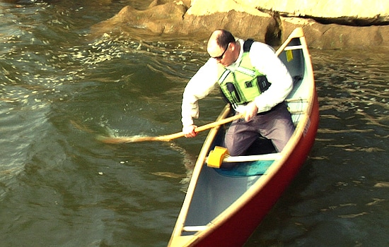 Man rafting into threatening baby wave near rock.