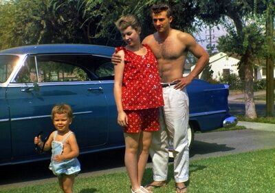 A man and woman standing in front of a blue car, taking care.