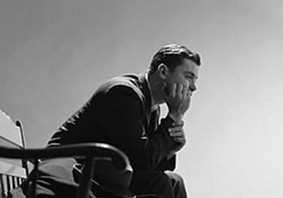 Black and white photo capturing a man's delayed gratification as he sits peacefully on a chair.