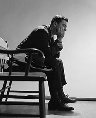 Black and white photo capturing a man's delayed gratification as he sits peacefully on a chair.