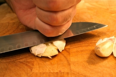 Man cutting garlic clove with knife. 