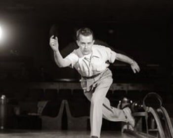 In this black and white photo, a man bowls a ball with precision and skill, aiming for a strike.