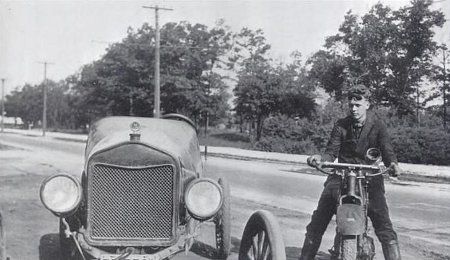 Charles Lindbergh sitting on motorcycle besides of car.