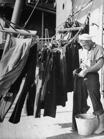 A man is washing denim clothes on the deck of a ship.