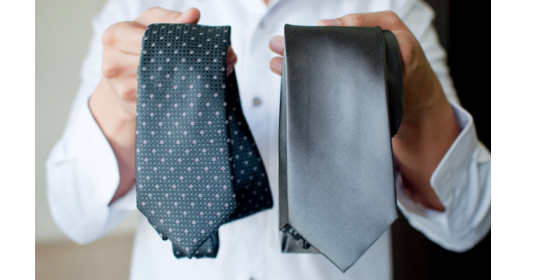 A man is holding two ties in front of a white background.