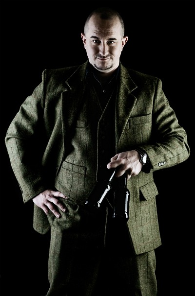 A brewmaster in a tweed suit holding a gun.