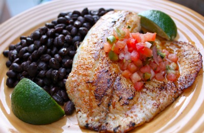 A plate with black beans cooked in a pot and a fish fillet fried in a pan.