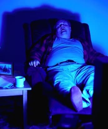 Man sleeping on chair with illuminating blue light. 