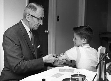 A young man in a suit is giving a boy a shot before heading out