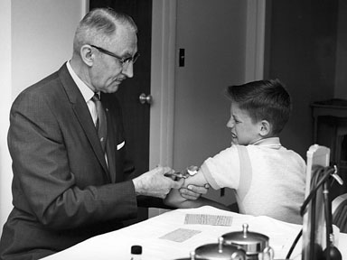A young man in a suit is giving a boy a shot before heading out