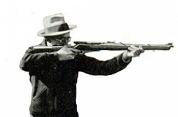 A man with a hat is holding a rifle, ready to shoot.