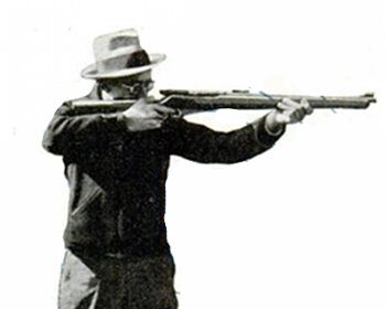 A man with a hat is holding a rifle, ready to shoot.