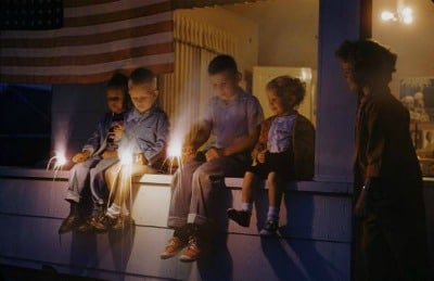 A group of children sitting on a porch on the 4th of July, enjoying traditional celebrations with candles.