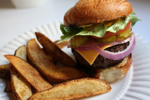 Gegrilde hamburger met frietjes in de papieren schaal.