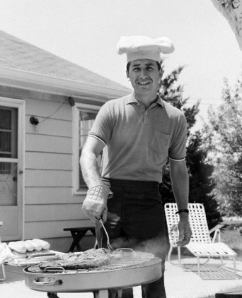 Vintage man wearing chef's hat grilling meat on patio.