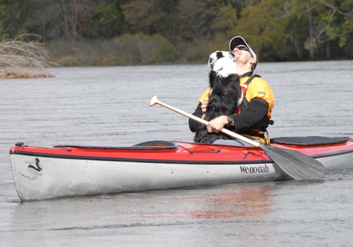 Dog jumping on man in the canoe.