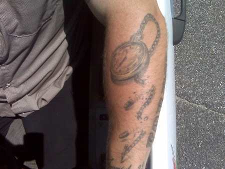 Tattoo of pocket watch with broken chain on arm.